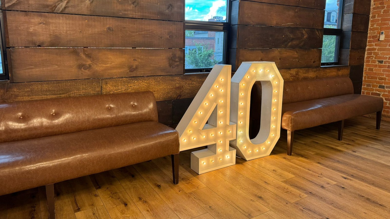 Two lit marquee numbers reading 40 standing at full height on a wood floor between two leather benches against a dark plank wall